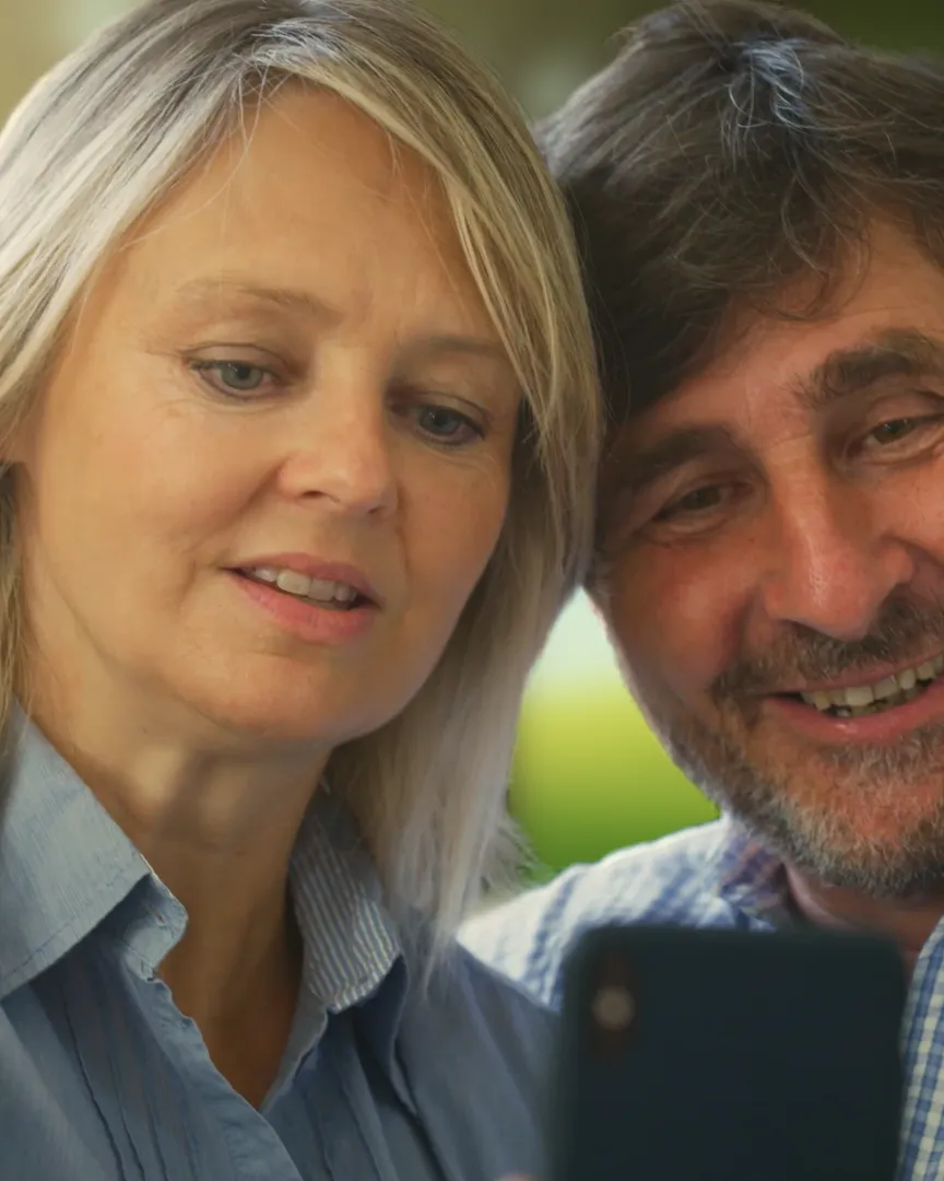 An older couple, cheek to cheek, smiling at one phone.